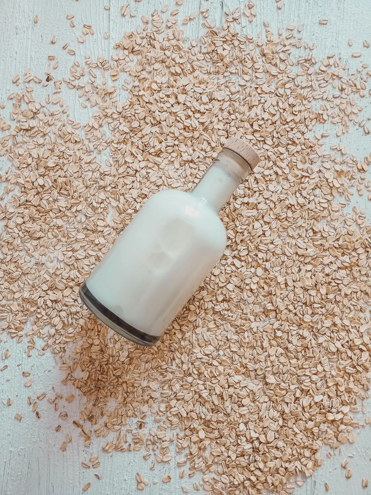 A glass bottle of oat milk lying on a bed of raw oats, evoking the plant-based pantry.